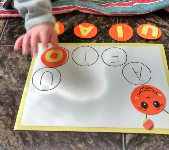 Mãos de uma criança encaixando vogais em uma prancha