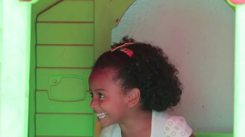 A Elis dentro da casinha do pátio, sorrindo e olhando para o lado