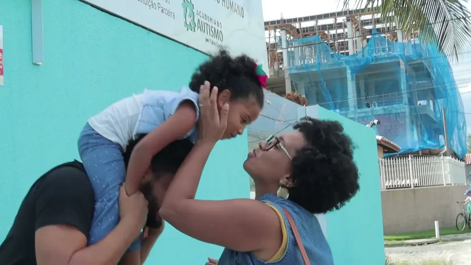 O pai carrega a filha nos ombros e a mãe sorri para ela, na porta da clínica